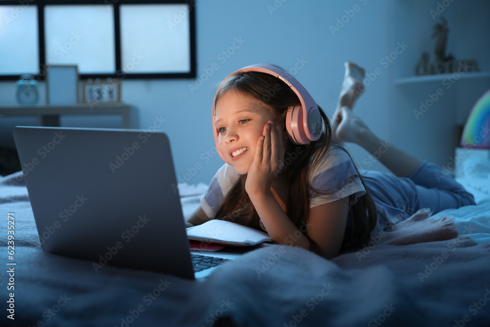 Little girl with headphones studying online in bedroom at night