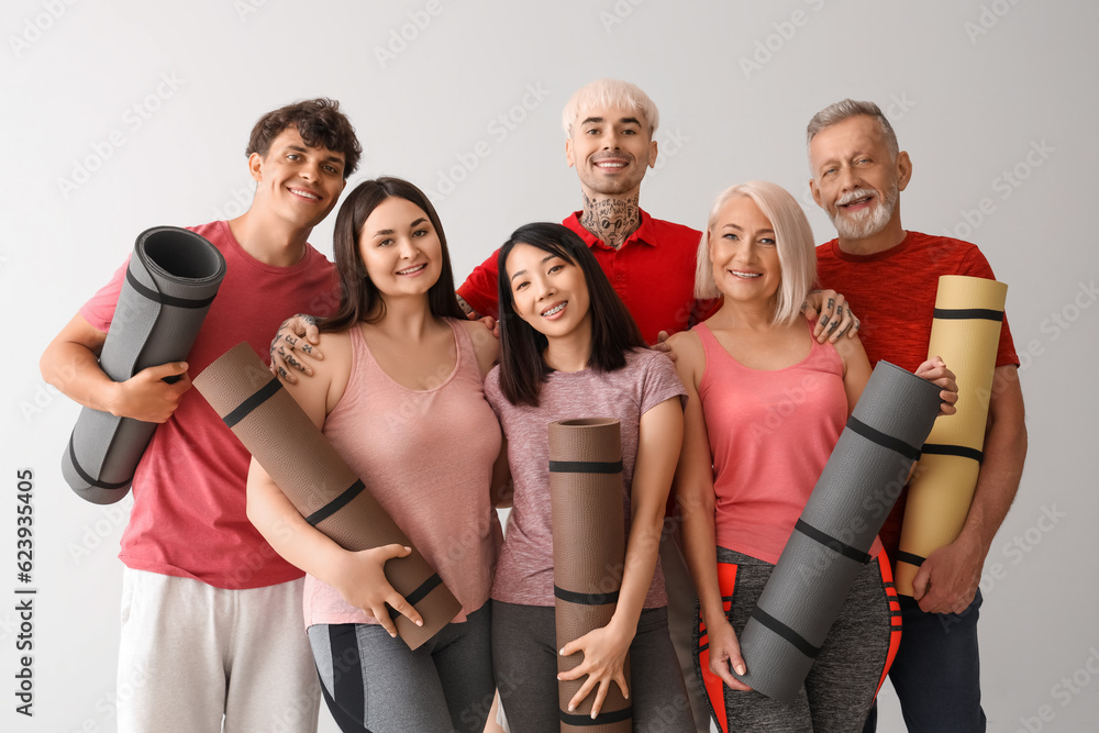 Group of sporty people with fitness mats on light background