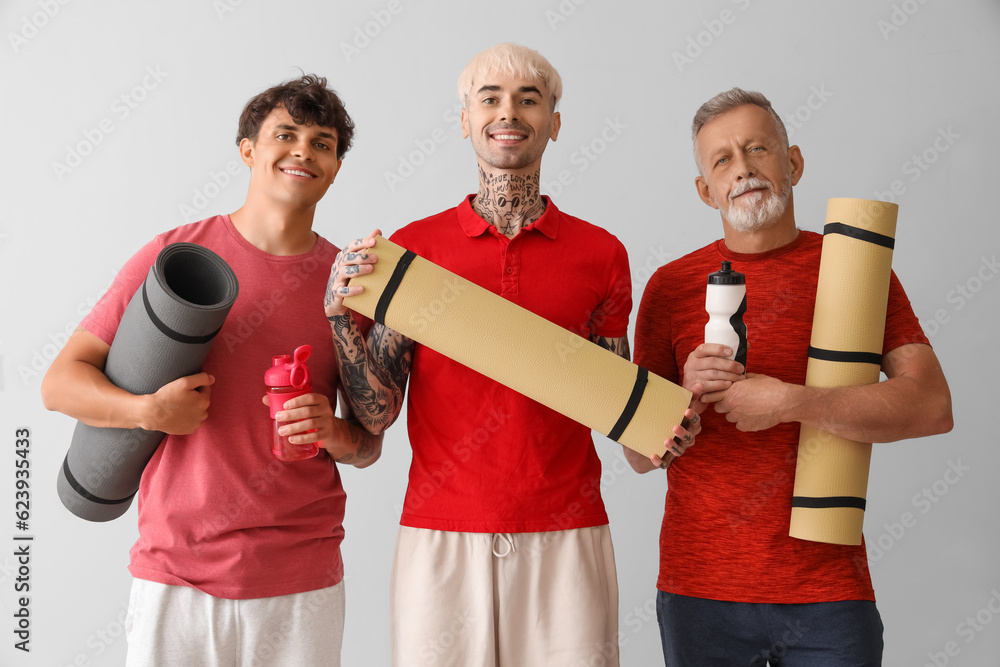 Sporty men with fitness mats and bottles of water on light background