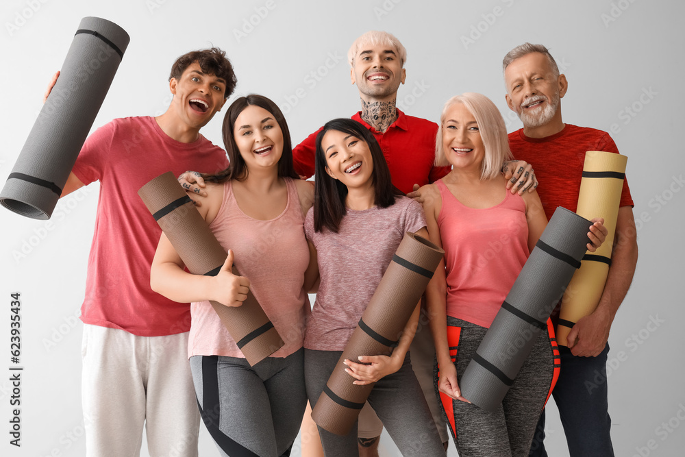 Group of sporty people with fitness mats on light background