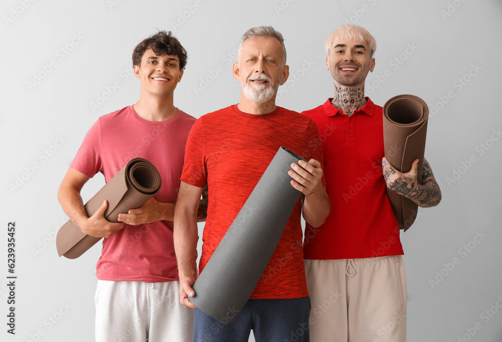 Sporty men with fitness mats on light background