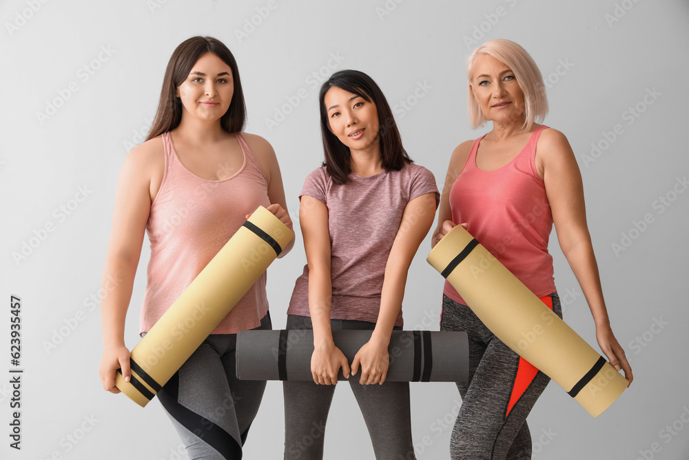 Sporty women with fitness mats on light background