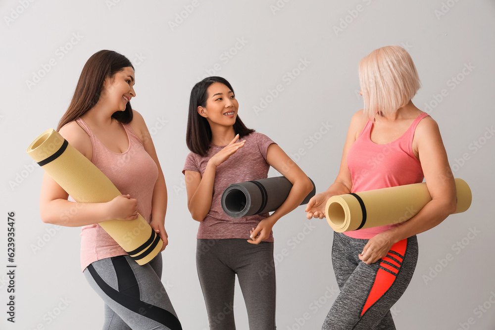 Sporty women with fitness mats on light background