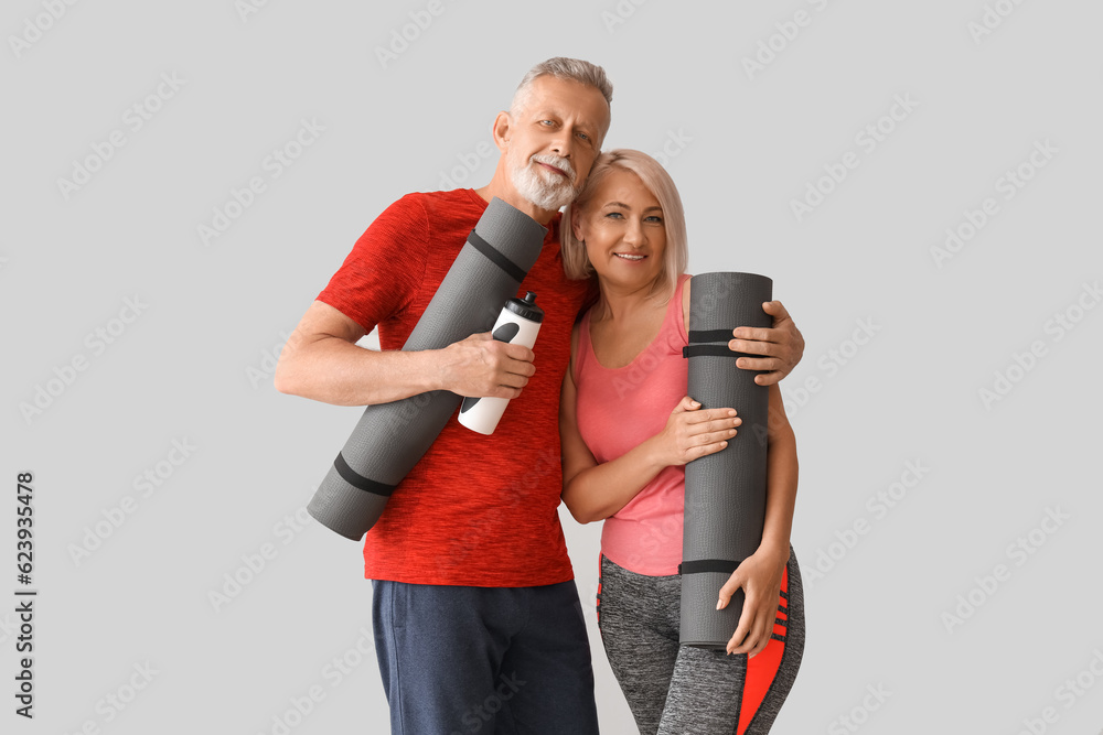 Sporty mature couple with fitness mats and water bottle on light background