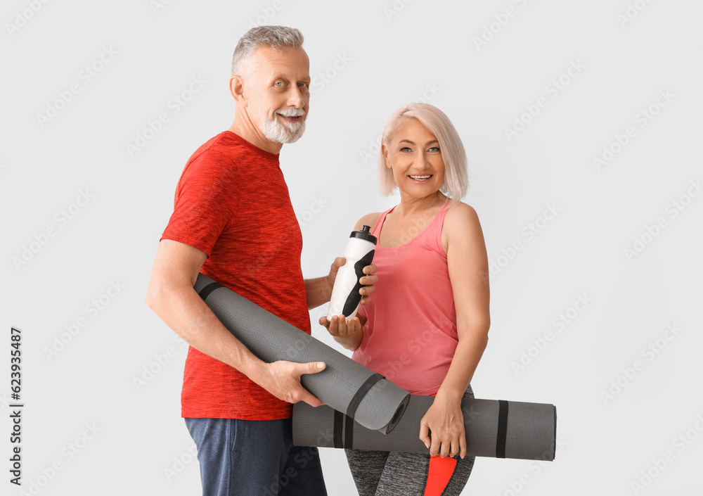 Sporty mature couple with fitness mats and water bottle on light background