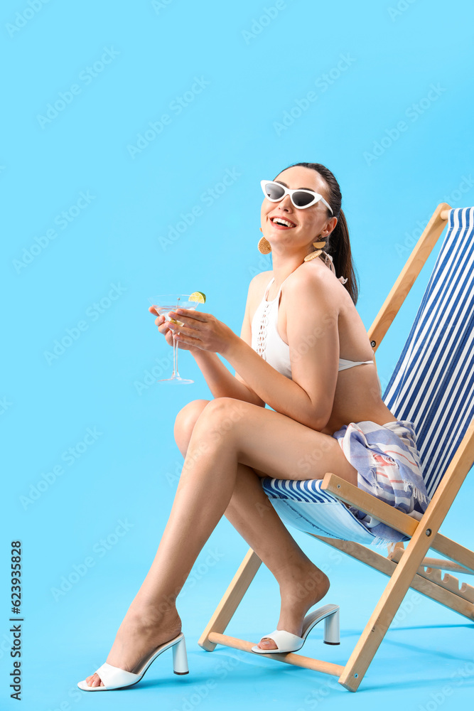 Beautiful woman in swimsuit with martini in deck chair on blue background