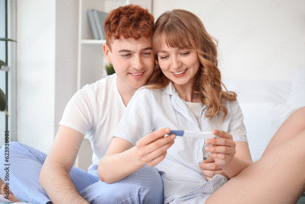 Happy young couple with pregnancy test in bedroom