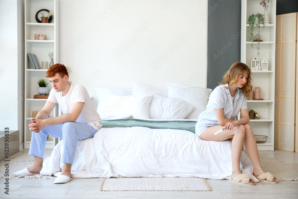 Sad young couple with pregnancy test in bedroom