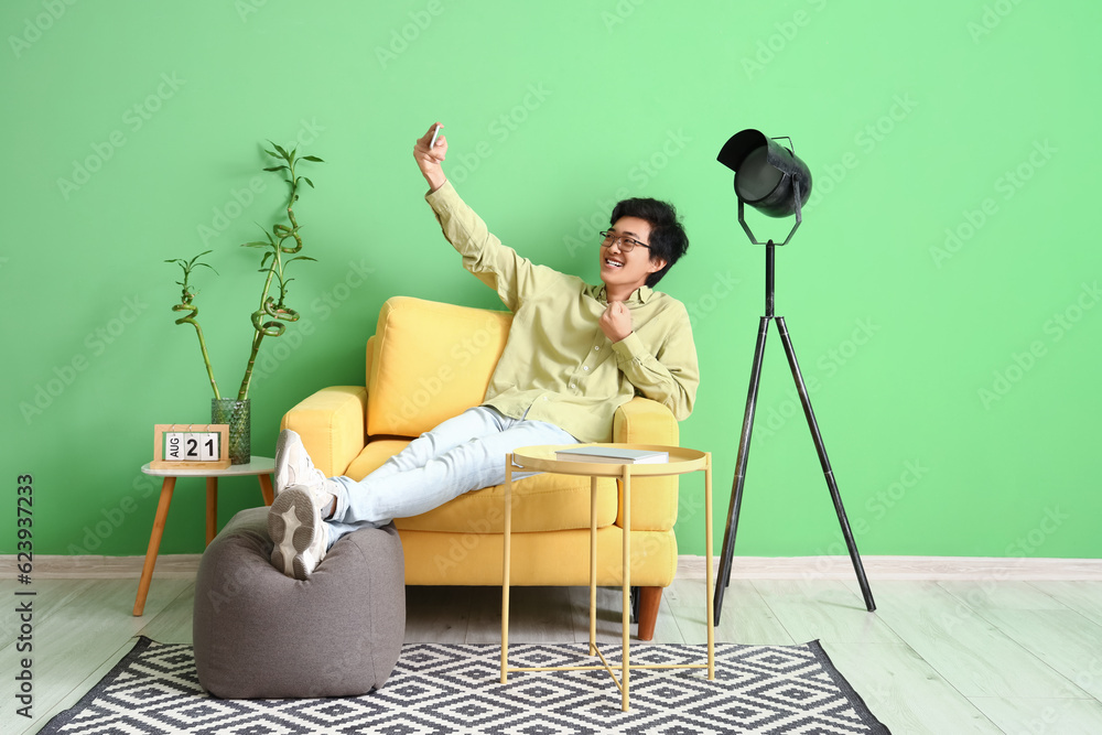 Young Asian man with mobile phone taking selfie on his day off at home