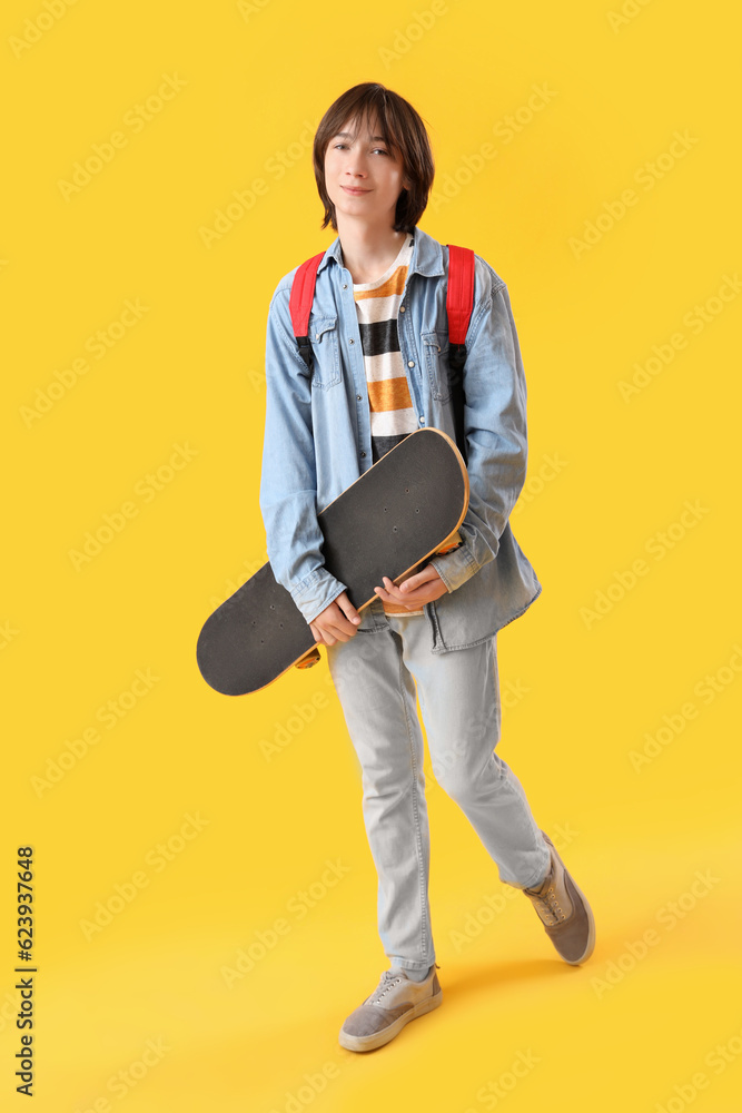 Male student with skateboard on yellow background