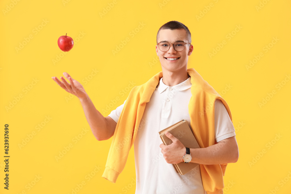 Male student with apple and books on yellow background