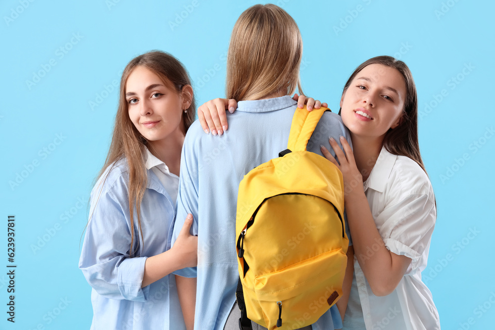 Female students hugging on blue background