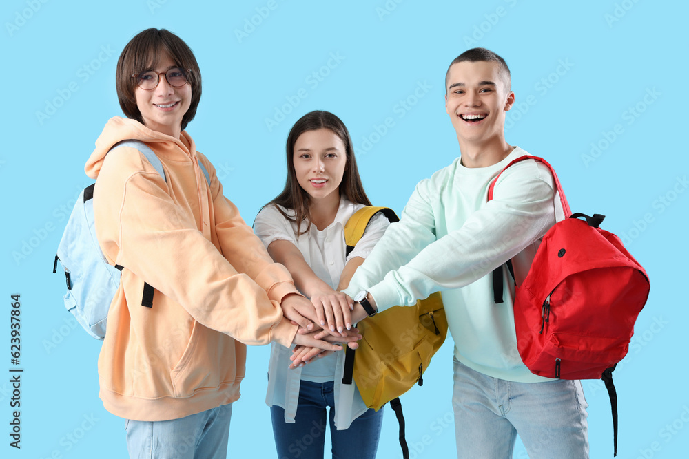 Teenage students putting hands together on blue background