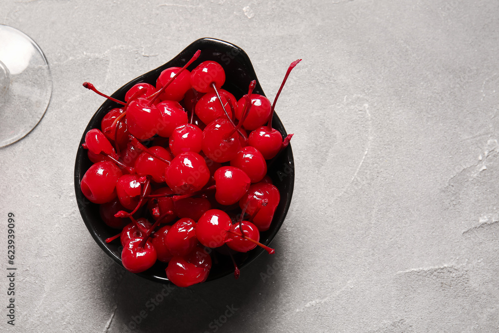 Bowl of tasty maraschino cherries on grey background