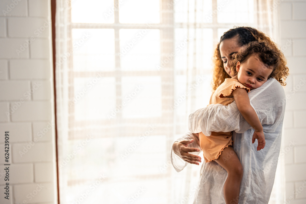 African American mother tosses young baby girl up in living room at home. 