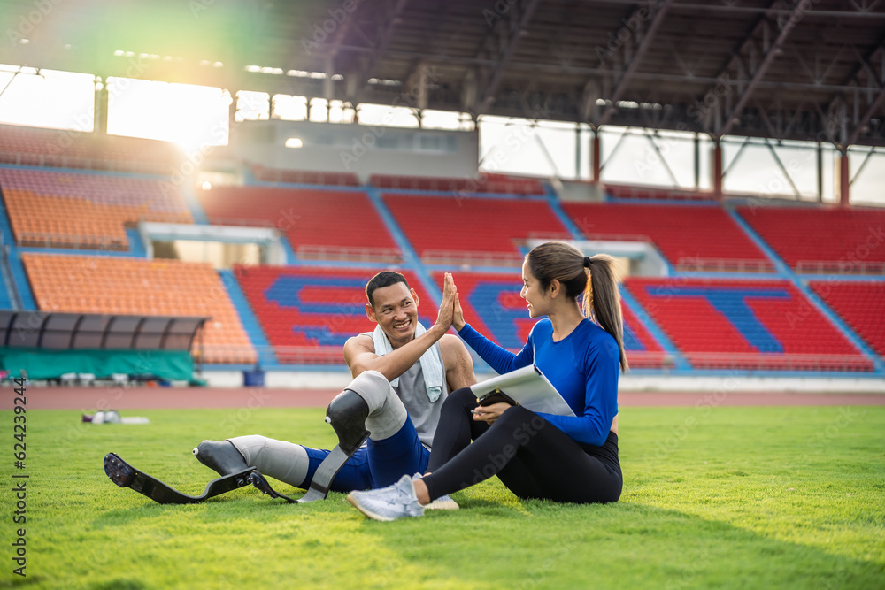 Asian para-athlete with prosthetic blades and trainer sit in stadium. 