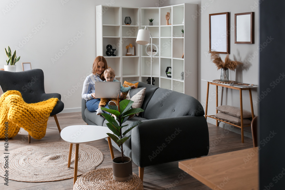 Beautiful woman with her little son and laptop on black sofa at home