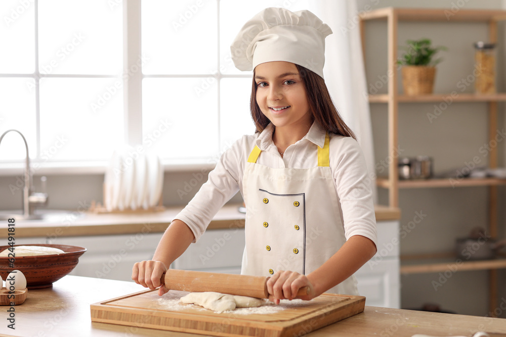 Little baker rolling out dough at table in kitchen