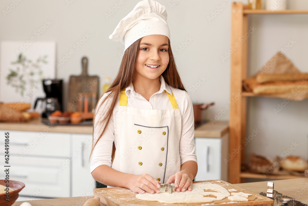 Little baker cutting dough for cookies in kitchen