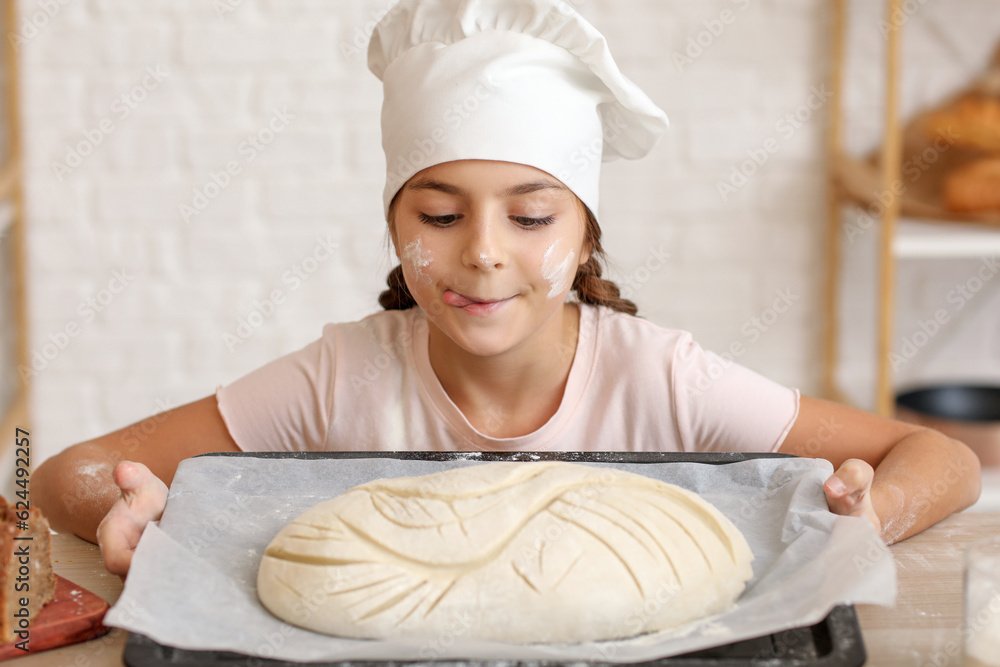 Little baker holding tray with raw bread in kitchen