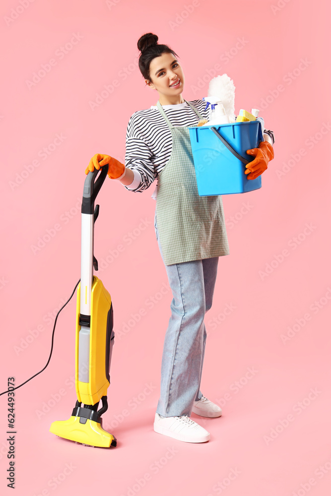 Young woman with cleaning supplies  on pink background