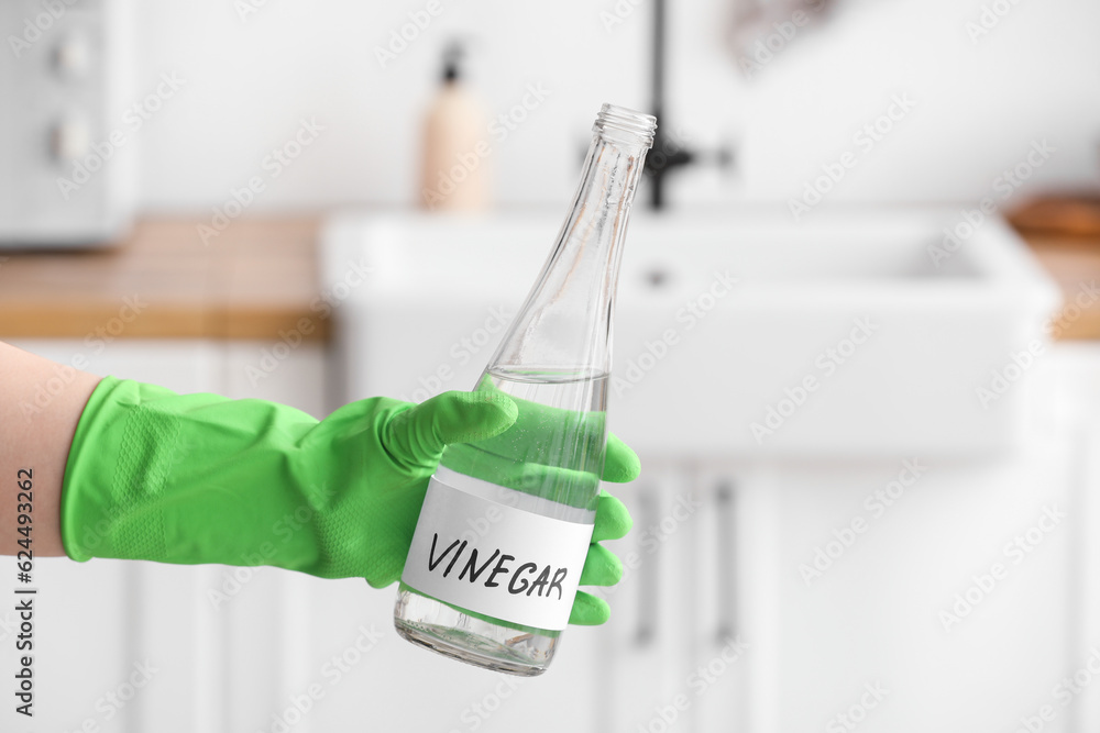 Female hand in rubber glove with bottle of vinegar in kitchen