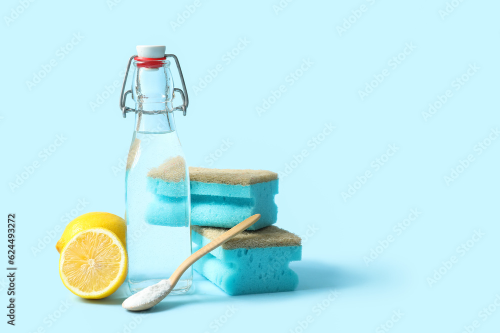 Bottle of vinegar, baking soda, sponges and lemons on color background