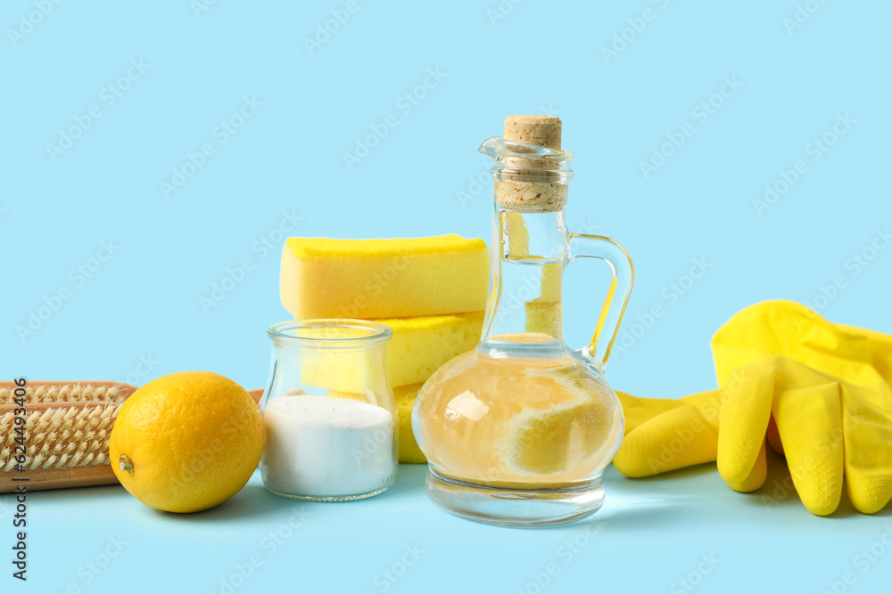 Jug of vinegar, baking soda, sponges, brushes, rubber gloves and lemon on color background