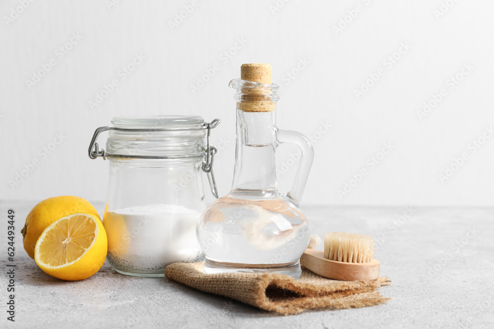 Jug of vinegar, baking soda, brush, napkin and lemons on table