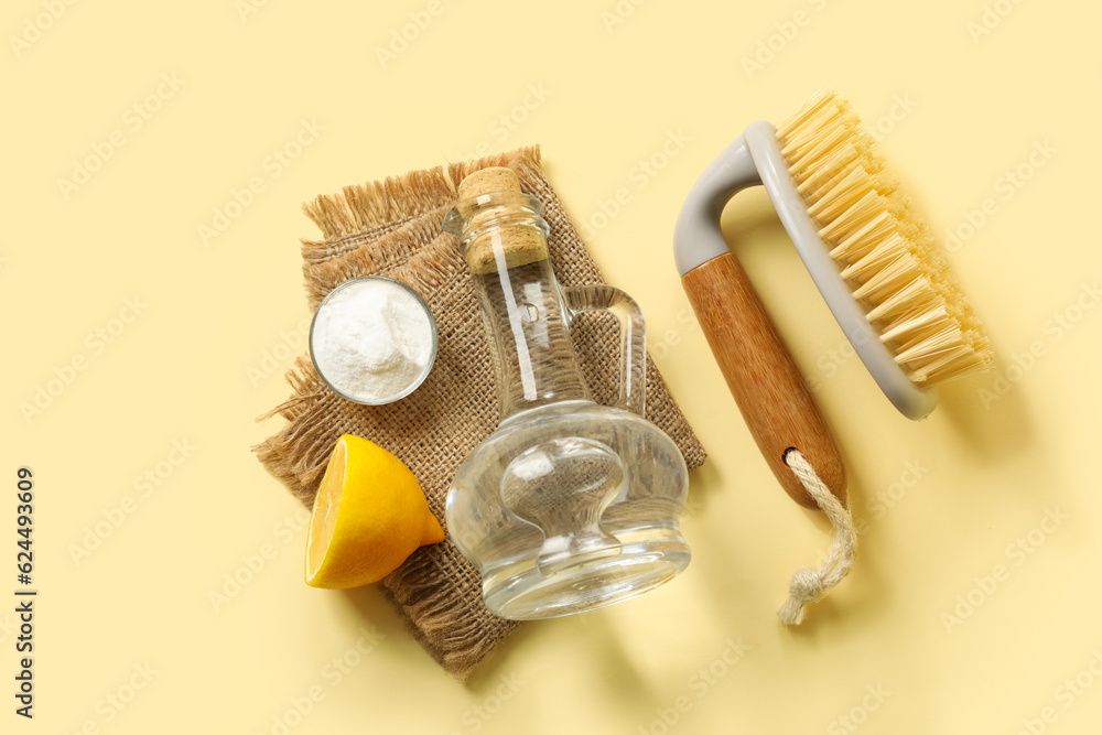 Jug of vinegar, baking soda, brush, lemon and napkin on color background