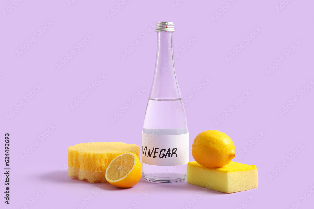 Bottle of vinegar, sponges and lemons on lilac background