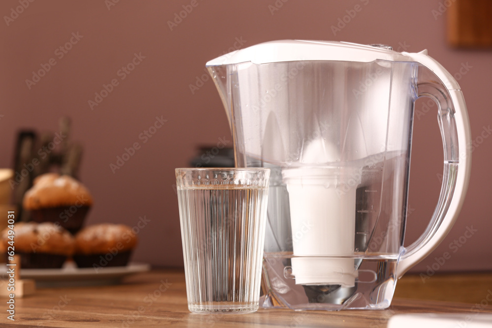 Glass of pure water and filter jug on wooden kitchen counter