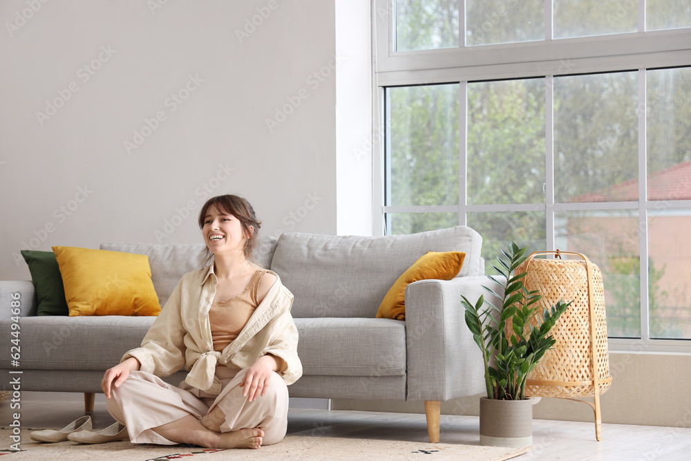 Pretty young woman lying meditating near grey sofa in light living room