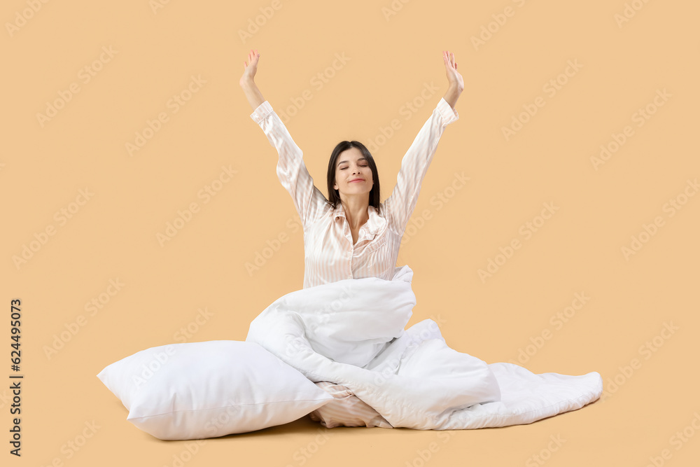 Awaking beautiful young woman with soft blanket and pillow on pale orange background