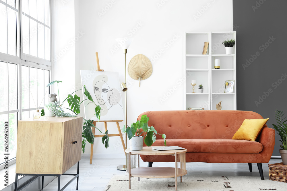 Interior of light living room with brown sofa and coffee table near big window