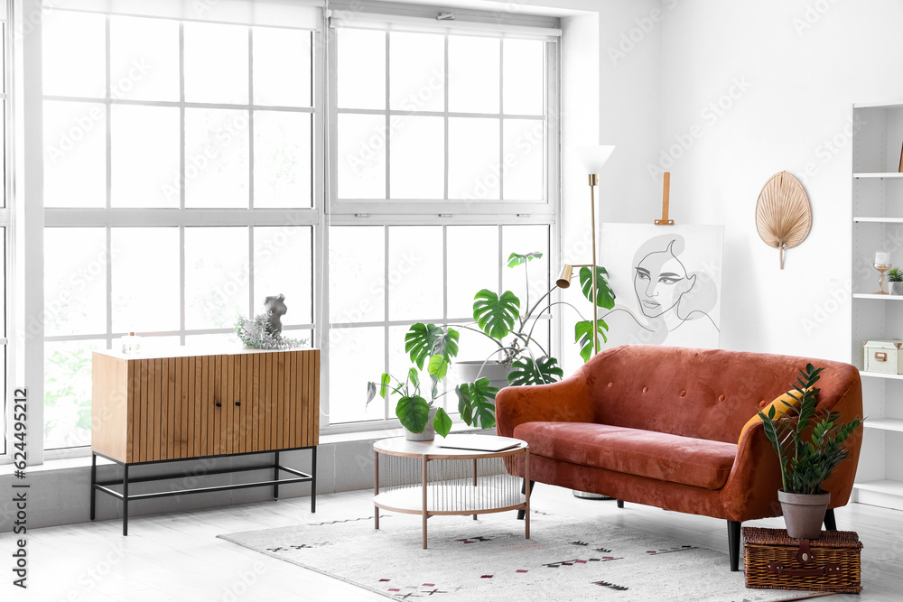 Interior of light living room with cozy brown sofa and coffee table near big window