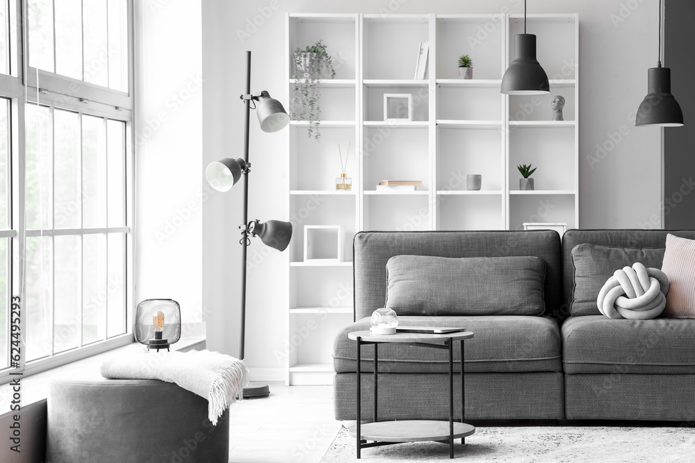 Interior of light living room with cozy grey sofa and coffee table near big window