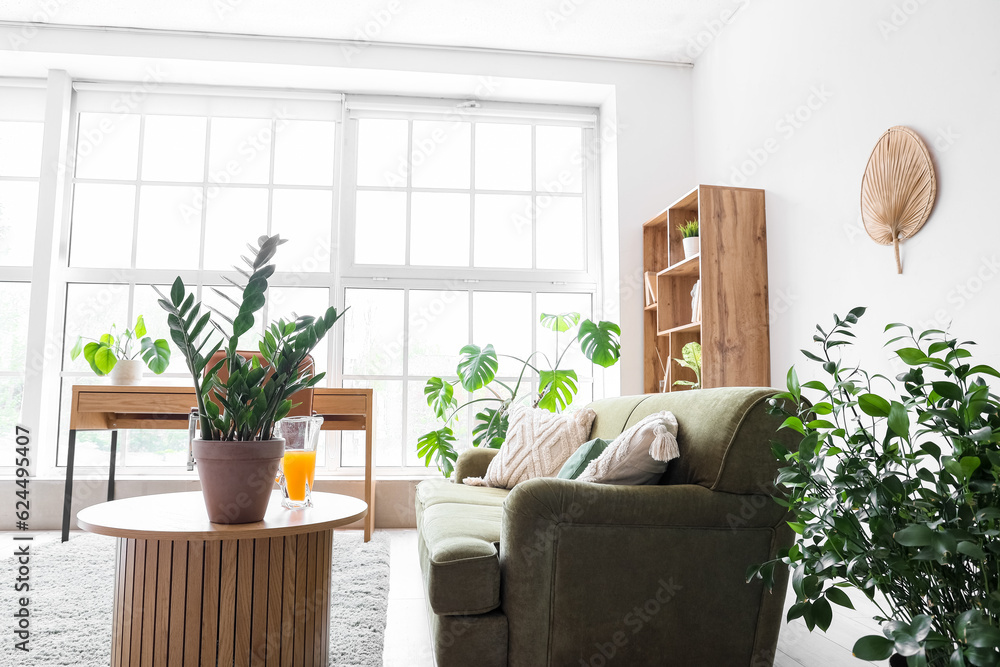 Interior of stylish living room with cozy green sofa and comfortable workplace near big window