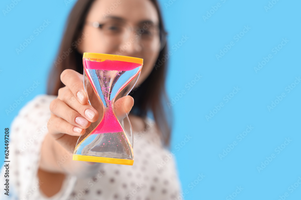 Young woman with hourglass on blue background, closeup. Deadline concept