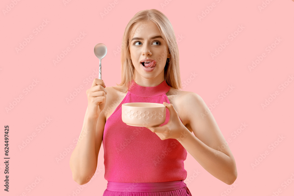 Young woman with spoon and bowl on pink background