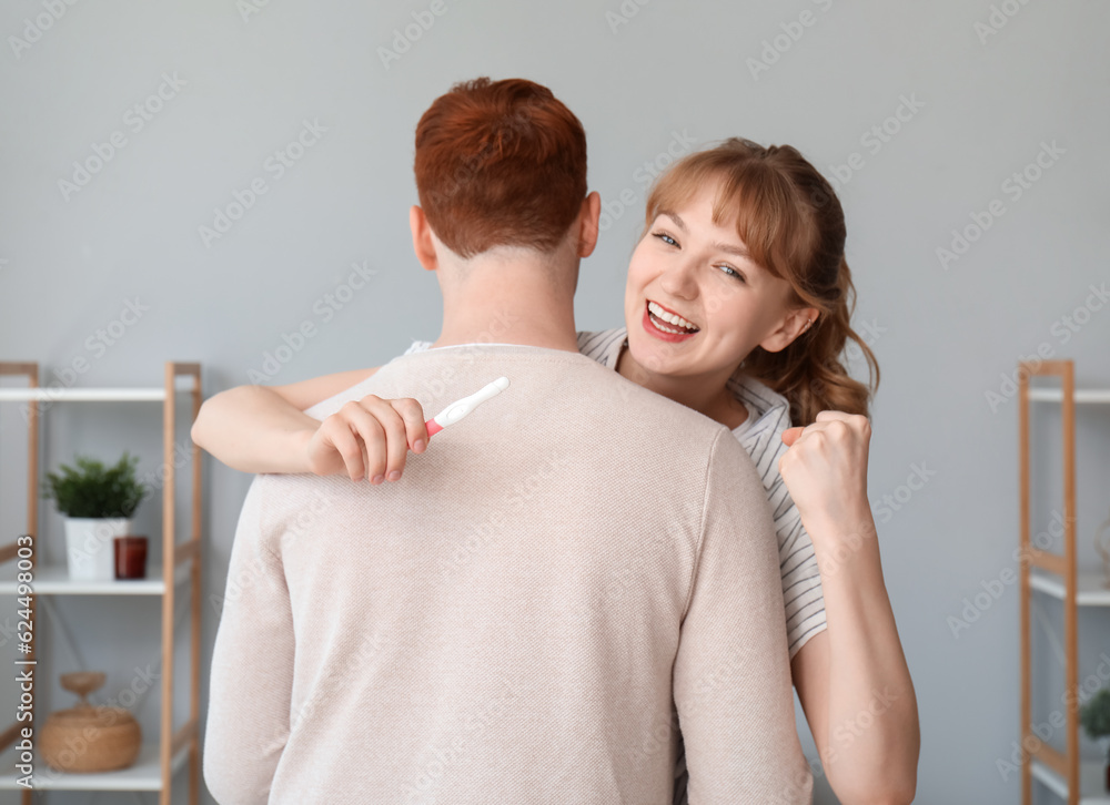 Happy young couple with pregnancy test hugging at home