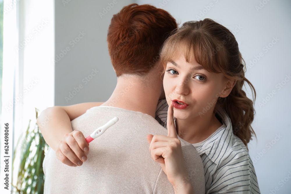 Young woman with pregnancy test showing silence gesture and her boyfriend at home, closeup