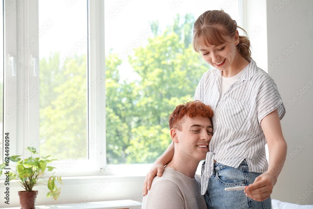 Happy young couple with pregnancy test hugging at home