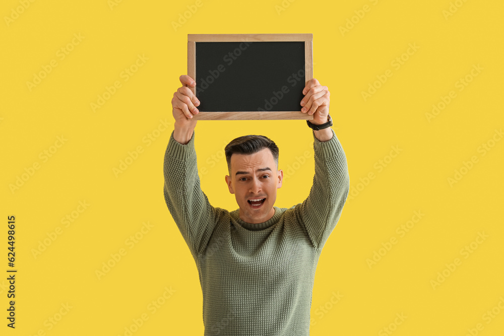 Stressed male teacher with chalkboard on yellow background