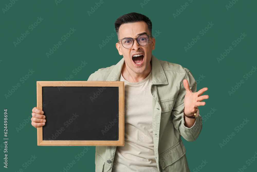 Angry male teacher with chalkboard on green background