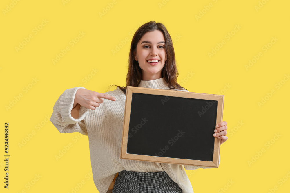 Female teacher pointing at chalkboard on yellow background