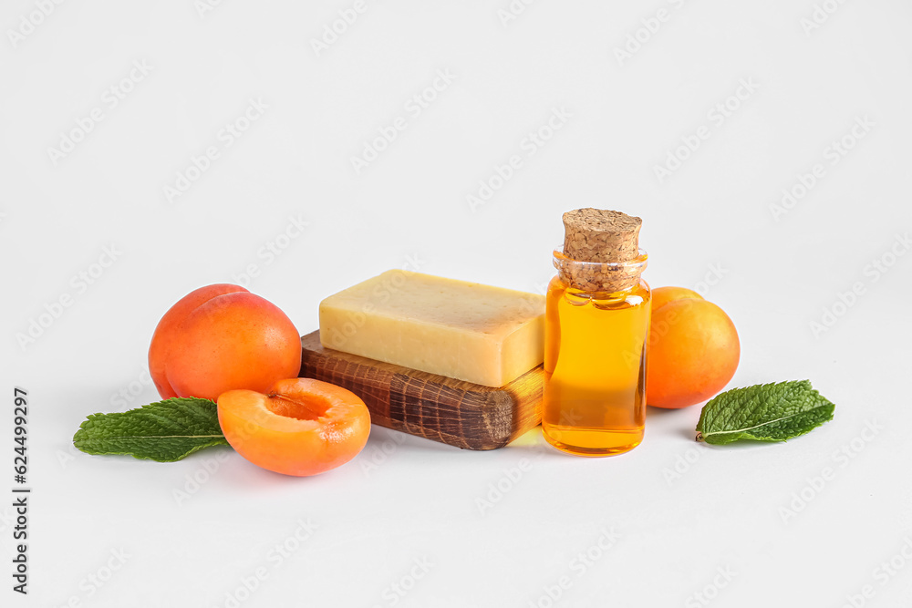 Bottle of essential oil, soap and apricots on white background