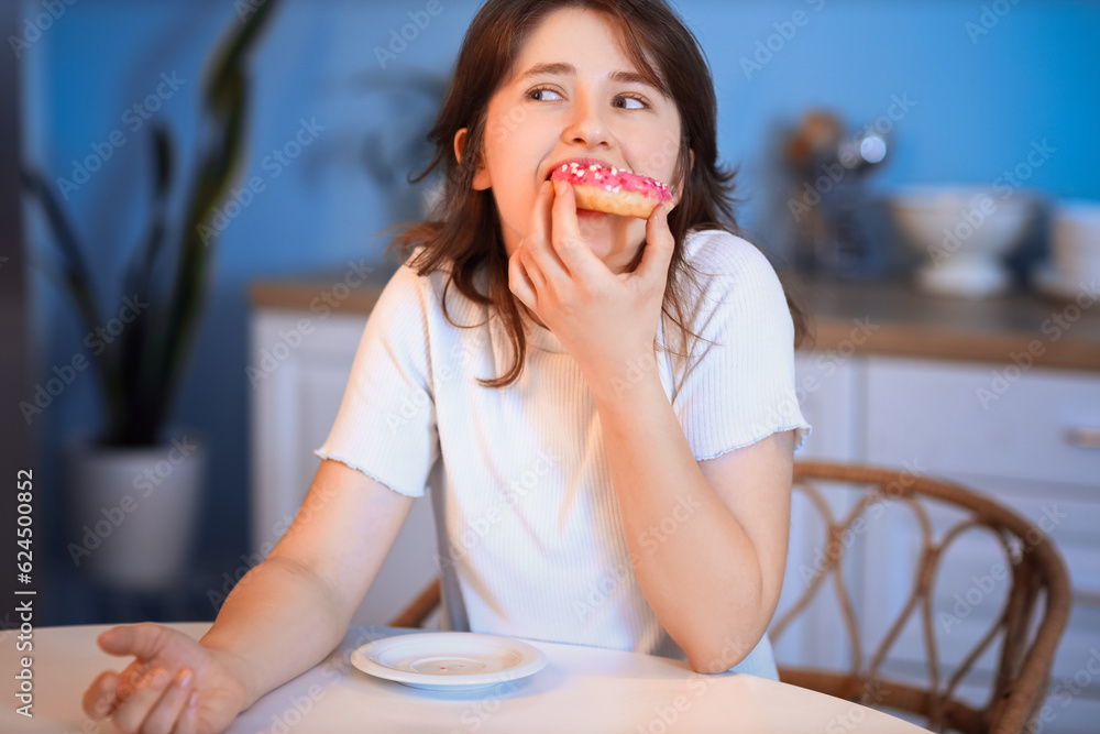 Young woman eating tasty doughnut in kitchen at night