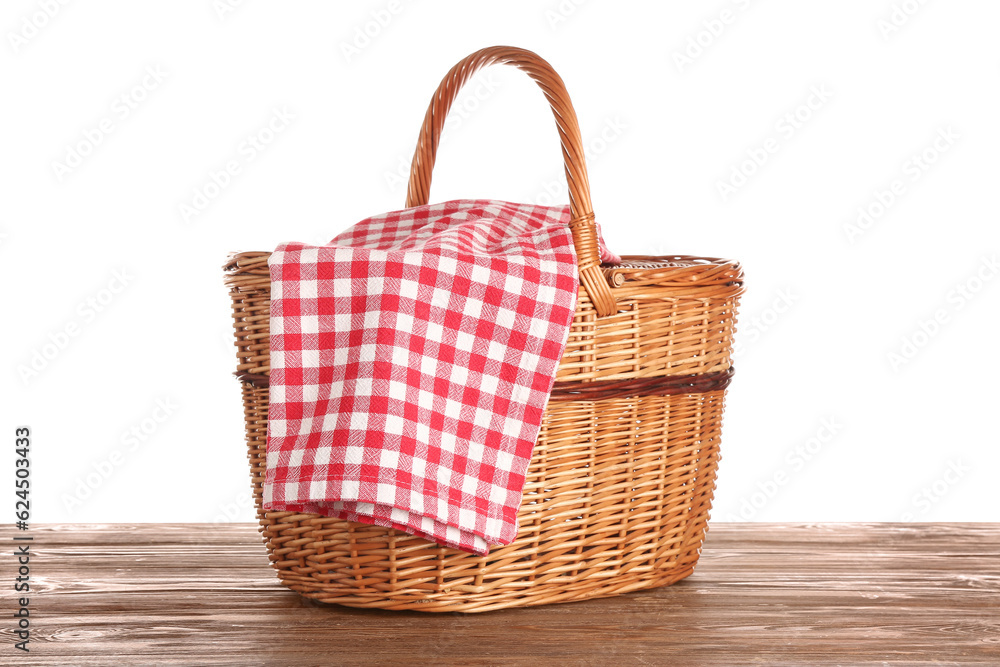 Wicker picnic basket with red checkered napkin on wooden table isolated on white background