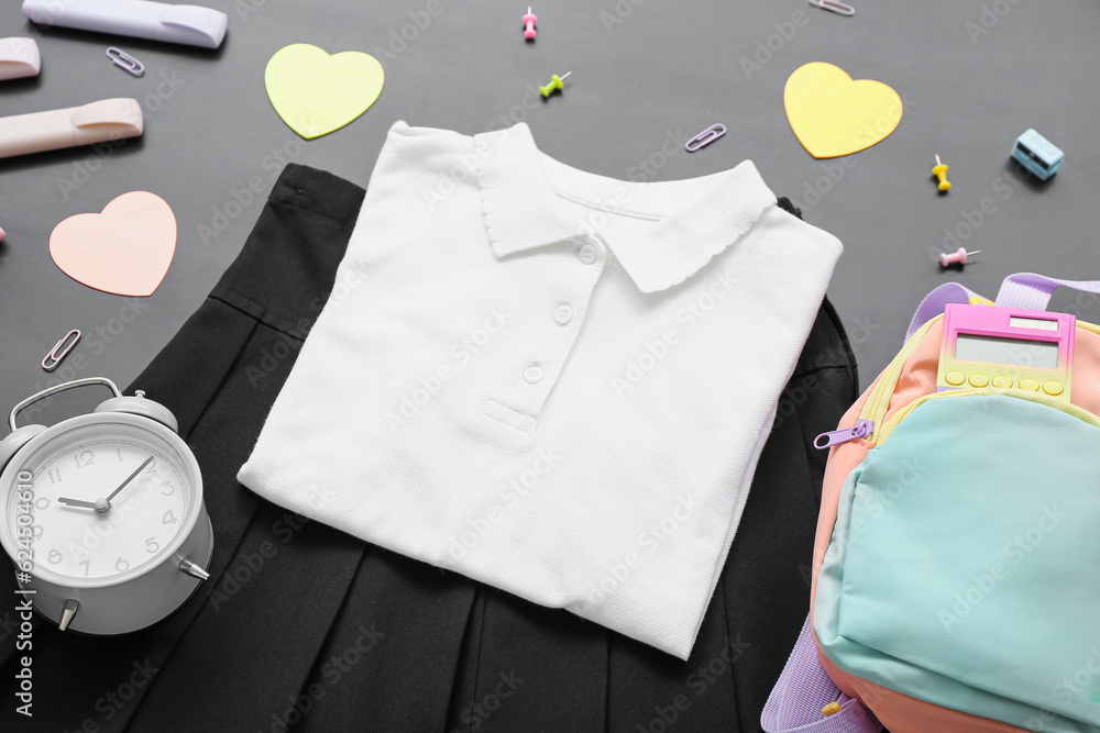 Backpack with different stationery and stylish school uniform on black chalkboard